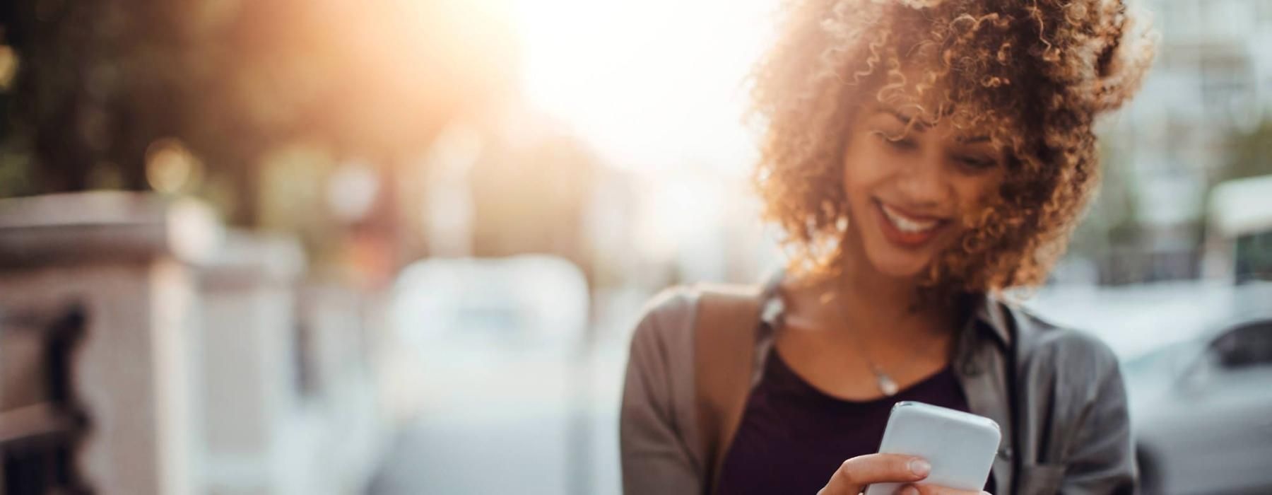 woman texts on her phone as she walks through the city